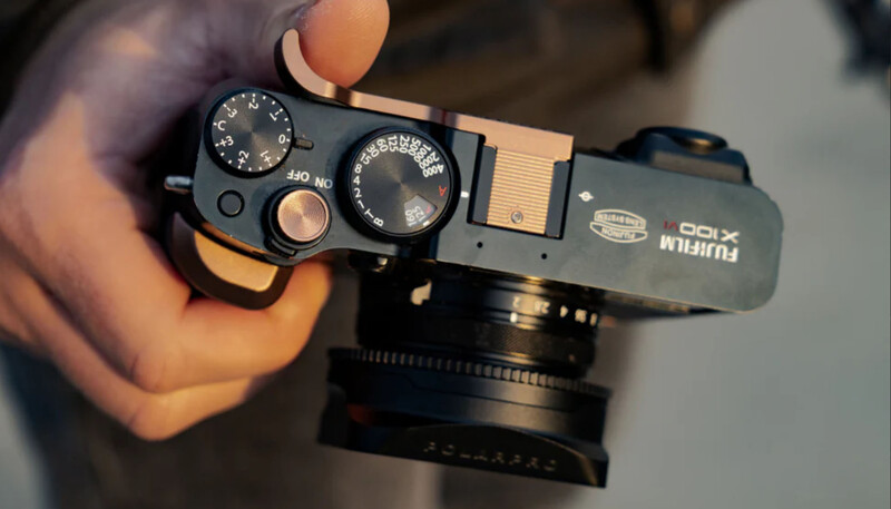 Hands holding a compact rangefinder camera with dual control dials and manual focus lens.