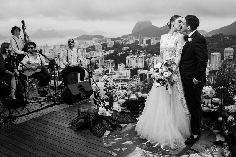 Bride and groom kiss during rooftop wedding ceremony with city skyline and mountains in background.