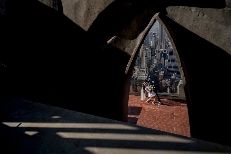 Framed view through a brick archway revealing a cityscape with tall buildings and a couple sitting on a terrace.