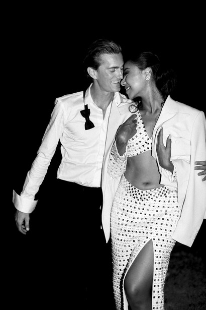 Two people in formal white jackets pose together against a dark background in black and white.