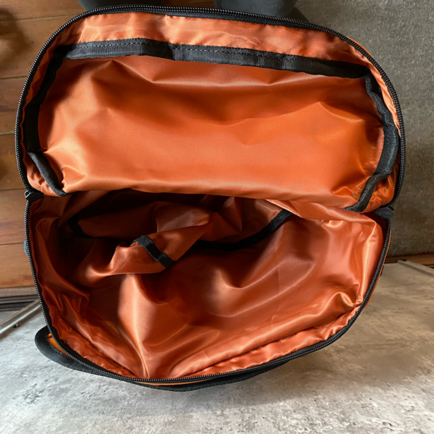 Open camera backpack with burnt orange interior compartments and black exterior material.