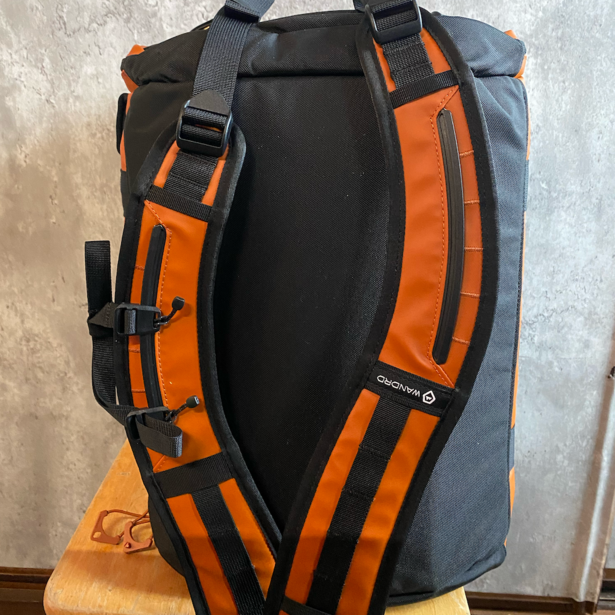 Back view of a gray and orange waterproof camera backpack with padded straps and side compression straps.