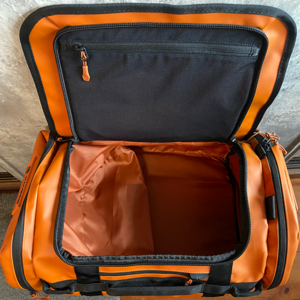 Orange and black camera bag with open lid, revealing black interior compartment and rust-colored fabric lining.