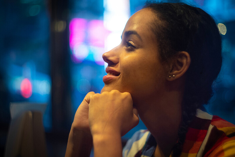 Woman in profile gazing thoughtfully at colorful city lights and neon signs at night.