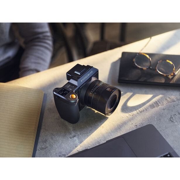 Black mirrorless camera with attached lens displayed on wooden table with accessories.