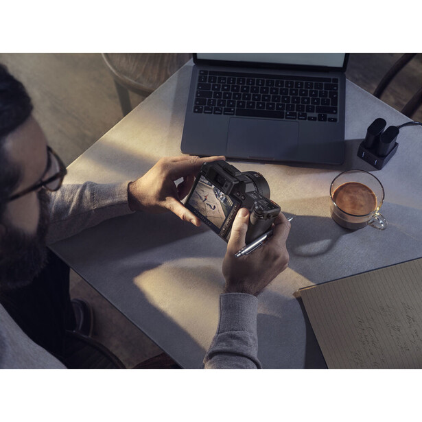 Photographer reviewing images on a camera display while working at a desk with a laptop and coffee.