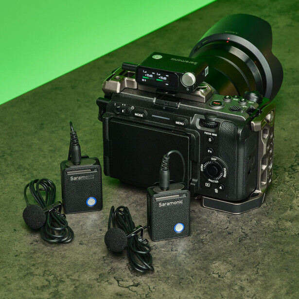 Professional camera with large lens mounted on a bright green background, surrounded by wireless microphone transmitters and receivers.