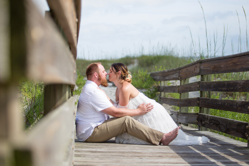 Example of capturing beach photography weddings in full sun, shows a couple kissing on a boardwalk in bright sunlight