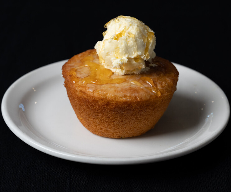 Warm pastry dessert topped with whipped cream on a white plate against black background.