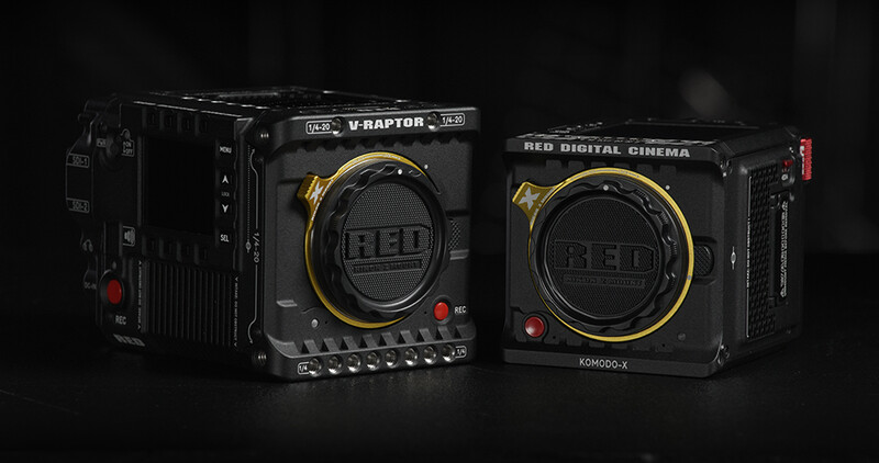 Two RED digital cinema cameras with black bodies and gold-accented lens mounts displayed against a dark background.