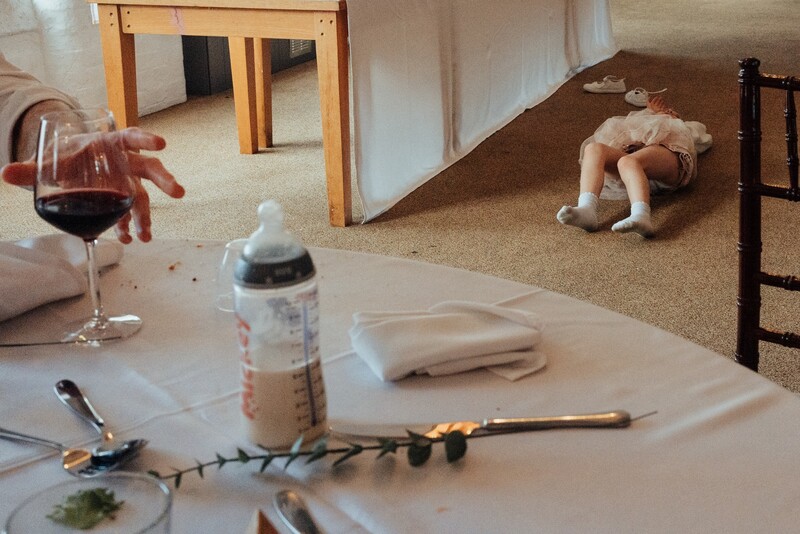 Styled flat lay with wine glass, baby bottle, and dining setup on white surface.