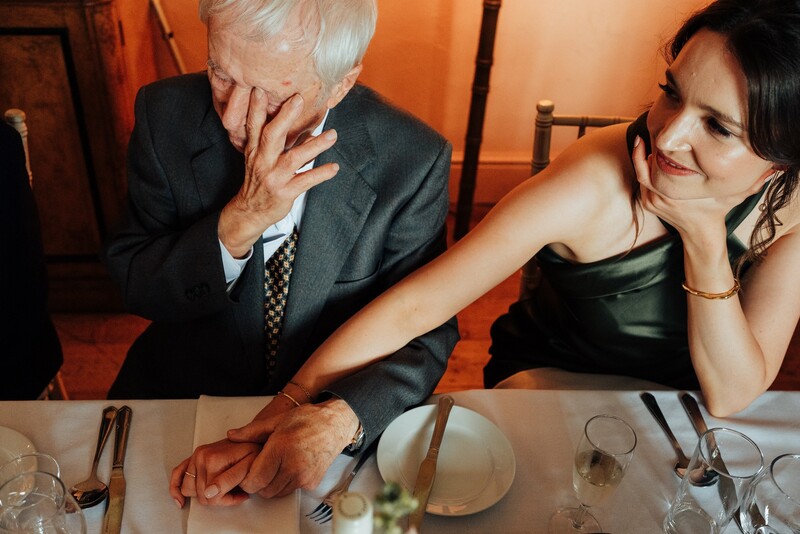 Older man in suit and younger woman at dining table, warm indoor lighting.