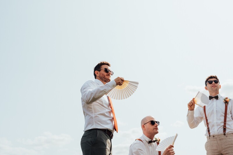 Three men in formal wear holding paper fans against a clear sky.