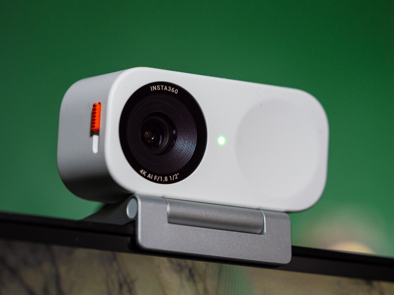 White and gray webcam with black lens mounted on adjustable bracket against green background.
