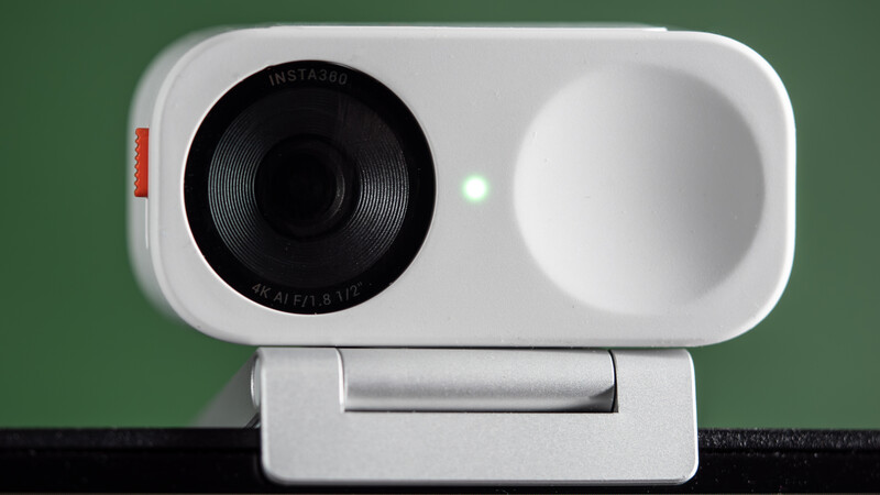 White webcam with black lens and silver mounting bracket against green background.