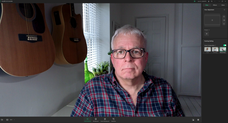 Screenshot of video call with man wearing plaid shirt and glasses, guitars visible on wall behind him.