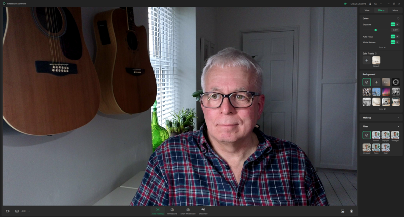 Man with glasses in plaid shirt seated at desk with acoustic guitars mounted on wall behind him.