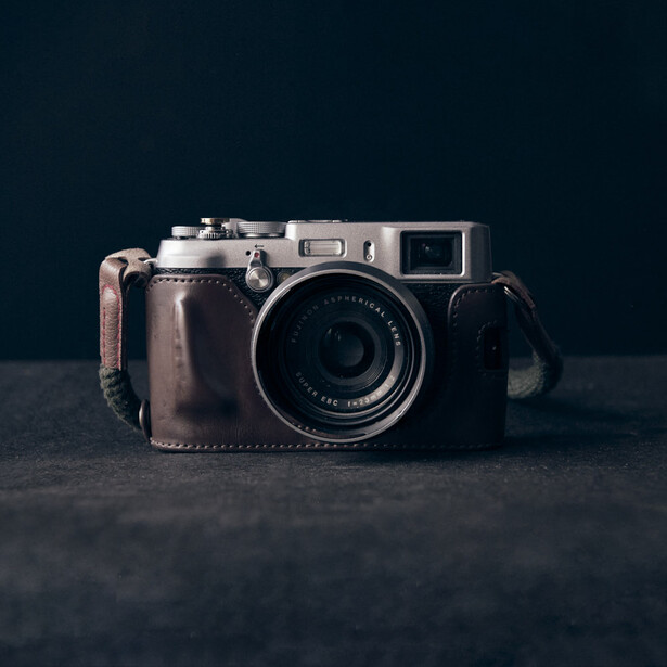 Vintage rangefinder camera with brown leather case against dark background.
