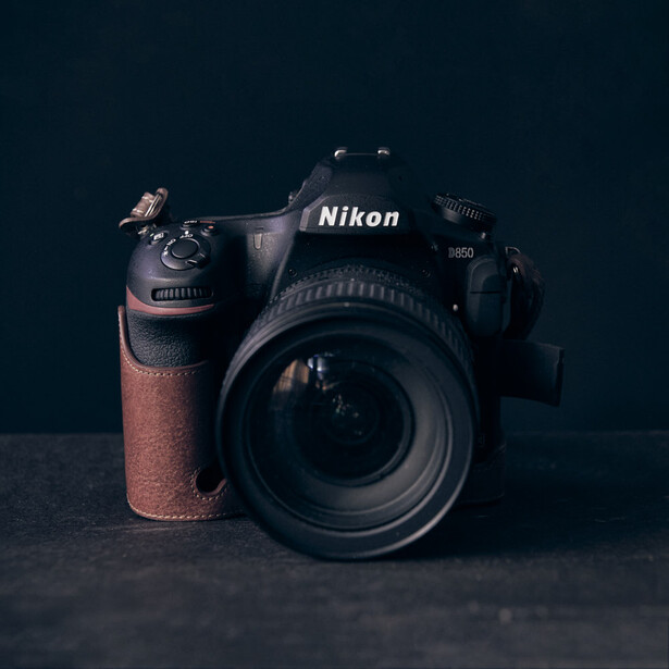 Nikon DSLR camera with telephoto lens on textured surface against dark background.