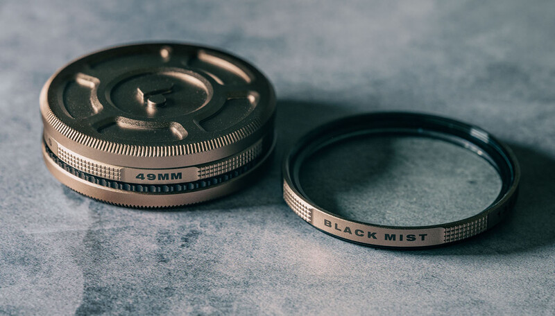 Two vintage camera lens filters with metal bands laid on a textured gray surface, one labeled 35mm and one labeled Black Mist.