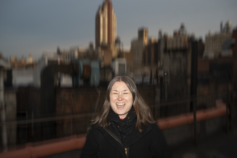 Woman with long dark hair smiling at camera with Westminster Palace blurred in background.