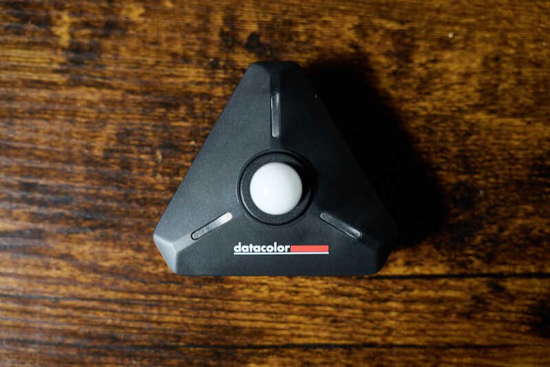 Datacolor spectrophotometer device on wooden surface with circular sensor window visible.