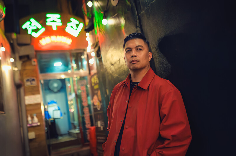 Man in red jacket standing in front of neon storefront signs at night.