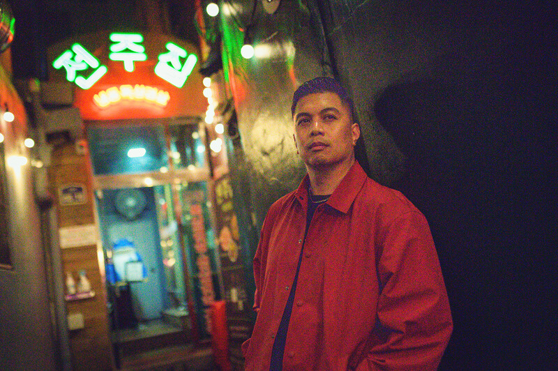 Man in red jacket standing in neon-lit urban alley at night.