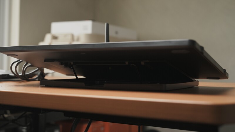 Black tablet computer positioned at an angle on a wooden desk surface with a coiled power cable.