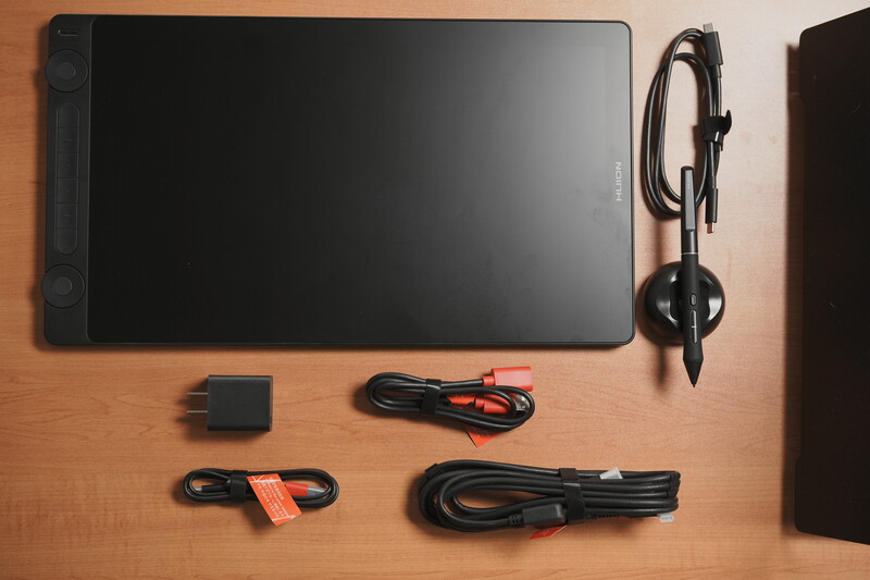 Digital drawing tablet with stylus pen and cables arranged on wooden surface.