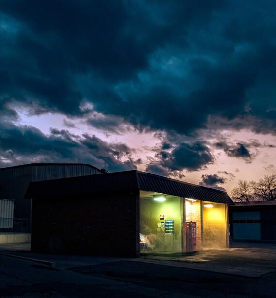 Illuminated small commercial building against dramatic stormy sky at dusk.