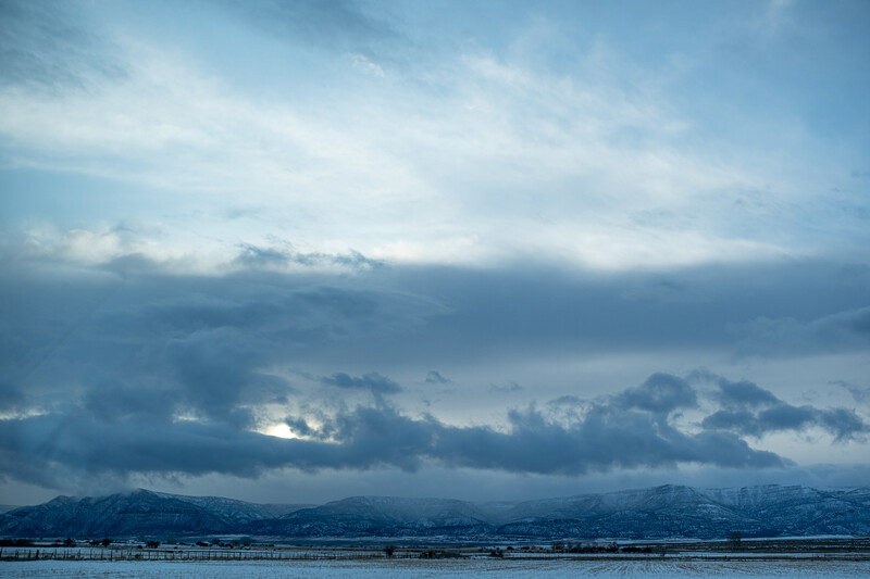 Dramatic cloudscape with snow-capped mountains beneath layered storm clouds and breaks of light.
