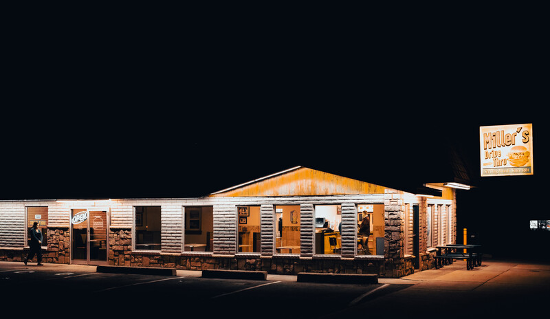 Nighttime photograph of a single-story building with wooden siding and a peaked roof, illuminated by warm lighting against a dark sky.