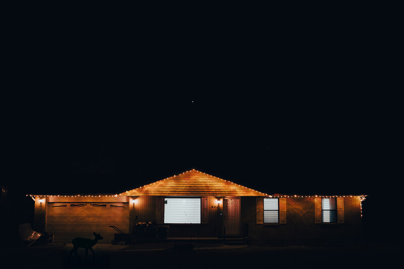 Single-story wooden house illuminated by warm exterior lighting against a dark night sky.