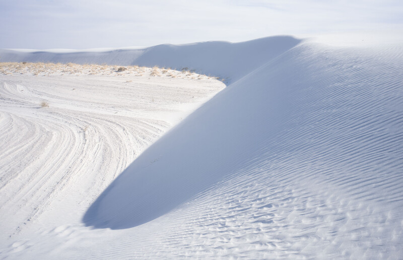 Wind-sculpted white sand dunes with sharp shadows and ripple patterns under bright daylight.