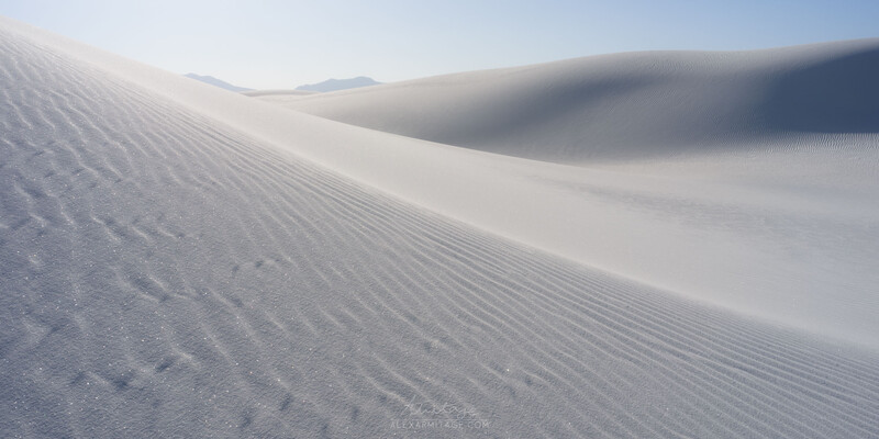 White sand dunes with rippled texture and subtle shadows under soft daylight.