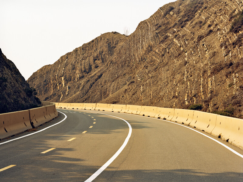 Modern highway curving through steep rocky canyon walls under warm afternoon light.