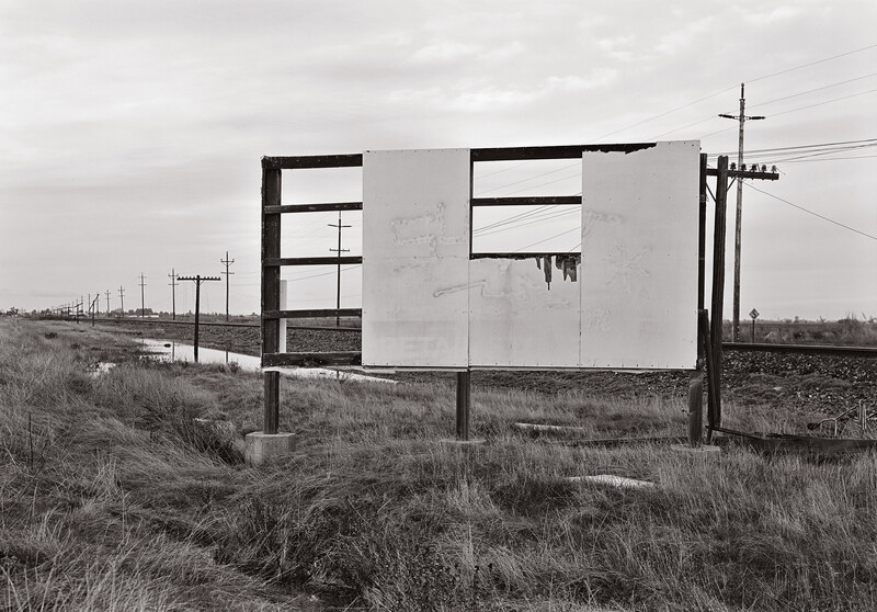 Abandoned roadside billboard with empty rectangular window cutouts standing in sparse grassland.