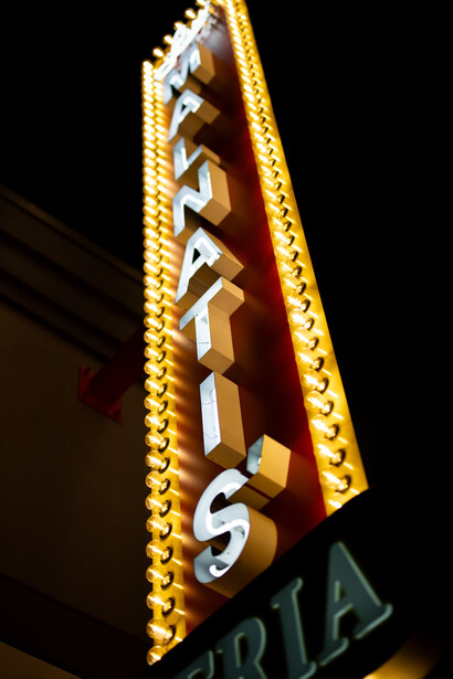 Vintage neon sign with yellow and red lettering mounted on building exterior at night.
