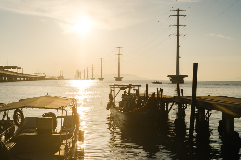 Silhouetted boats docked at a wooden pier during golden hour with utility poles lining the distant waterfront.
