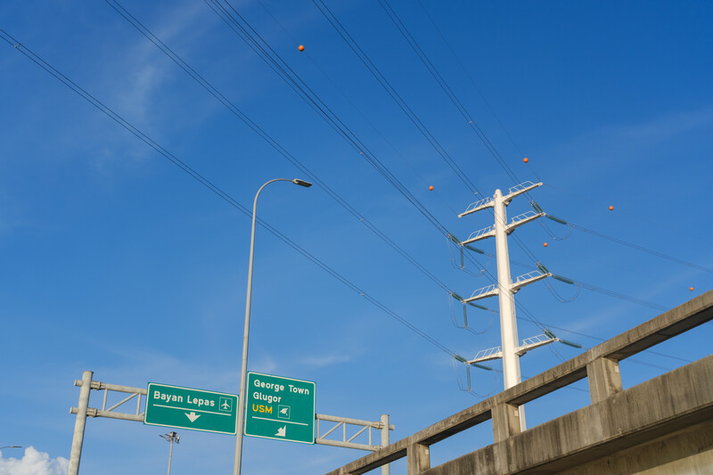 Highway overpass with green directional signs and power lines against clear blue sky.
