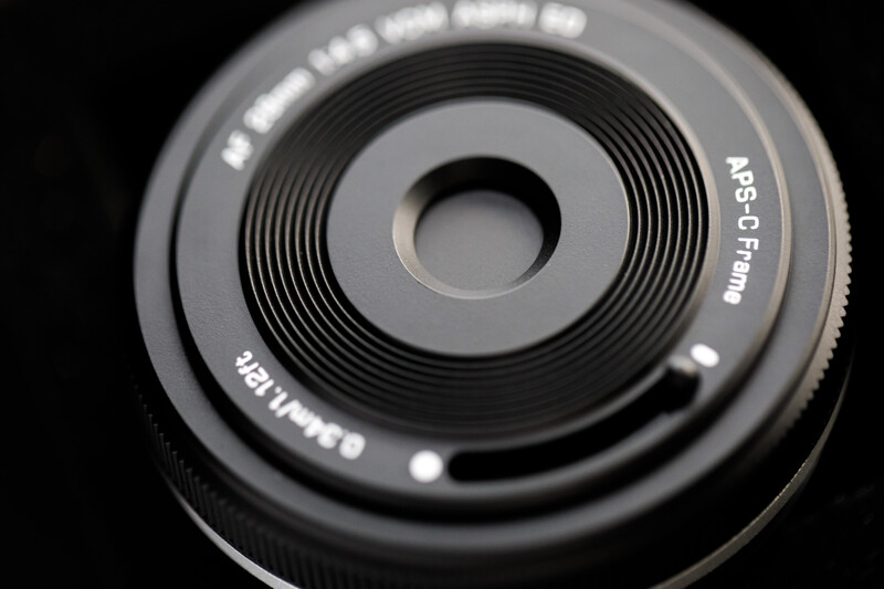 Close-up view of a camera lens front element showing concentric focus ring grooves and aperture markings.