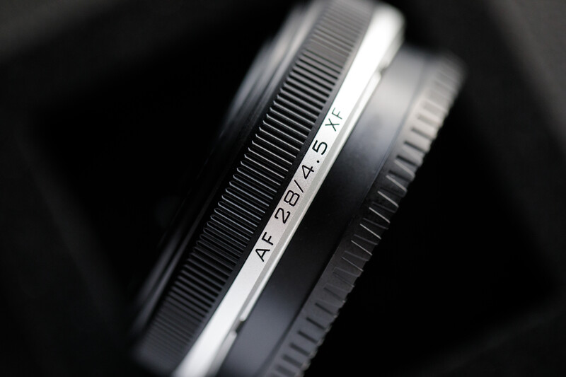 Close-up of camera lens barrel showing focal length markings and focus ring details in black and white.