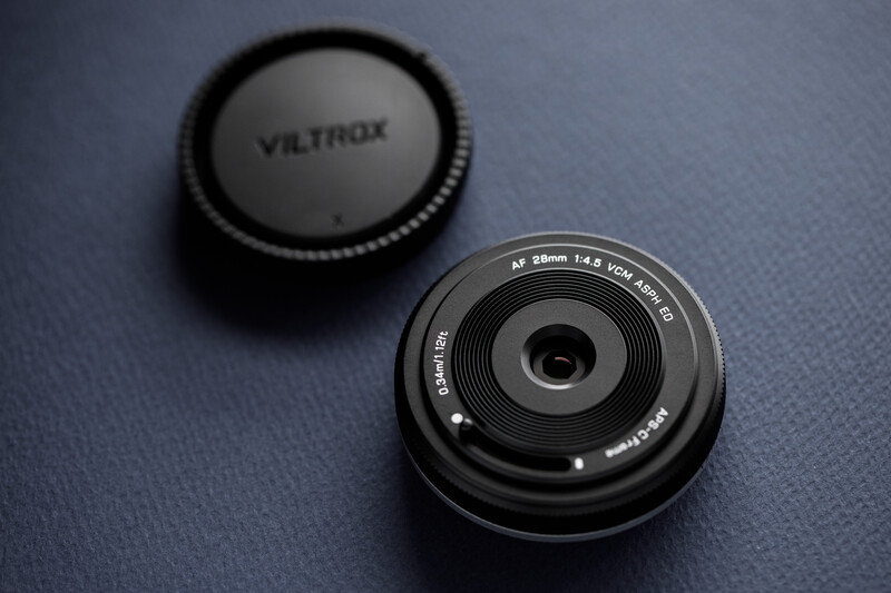 Viltrox 35mm f/1.4 lens with rear cap on blue surface, showing front element and aperture blade details.