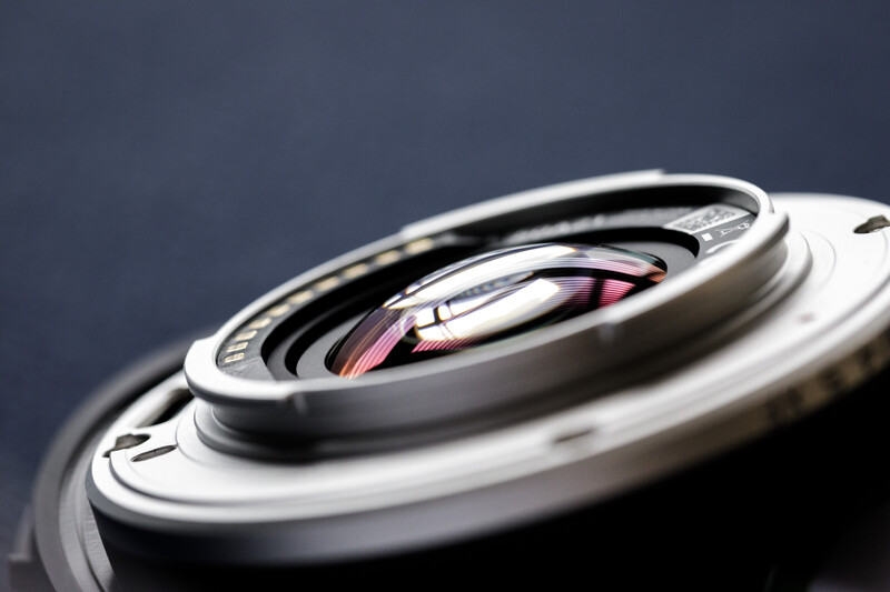 Close-up macro photograph of camera lens elements showing internal glass optics and pink reflections.