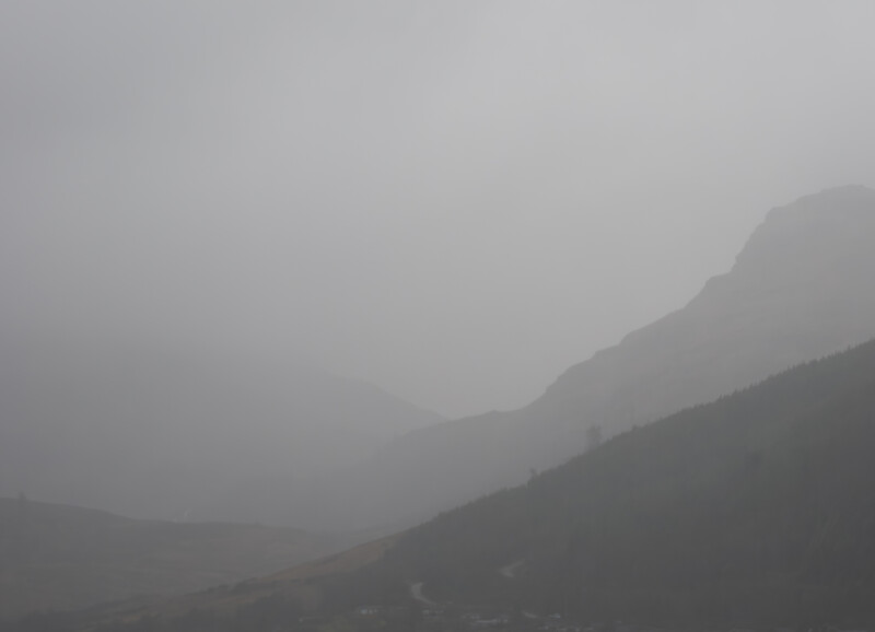 Mountainous landscape shrouded in thick fog and mist, with layered ridges fading into dense clouds.