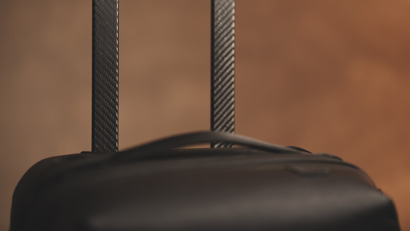 Close-up of a black camera bag with dual gray fabric handles against a warm brown background.