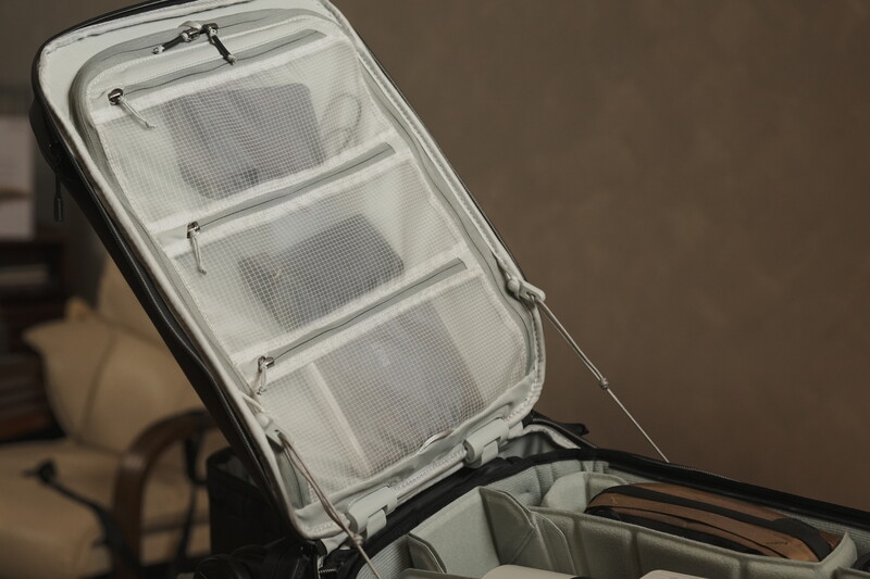 Open packing cube with white mesh compartments and black straps inside a larger travel bag.