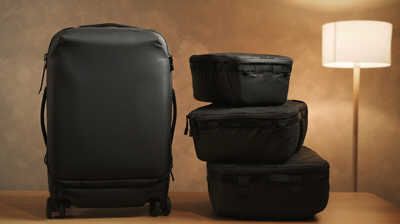 Black travel luggage and packing cubes arranged on a wooden surface with warm ambient lighting.
