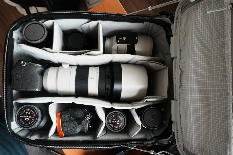 Camera bag interior with organized compartments holding telephoto lens, camera body, lenses, and accessories.